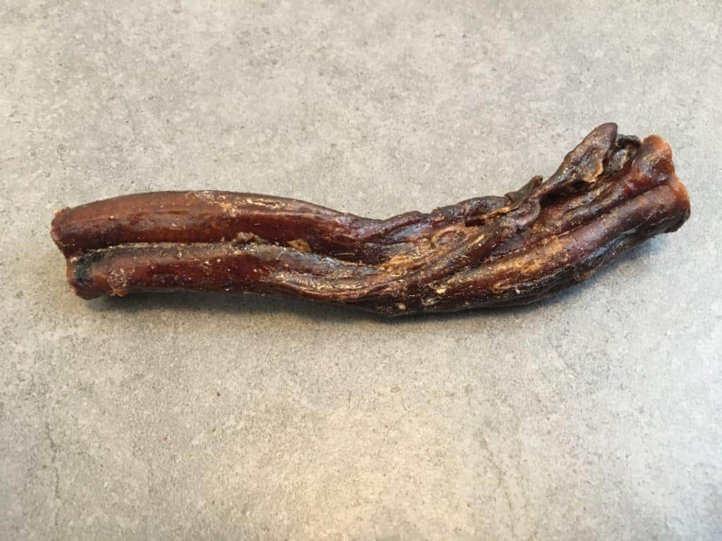 Ein einzelnes gedrehtes Stück braunes Beef Jerky auf einer grau strukturierten Oberfläche.