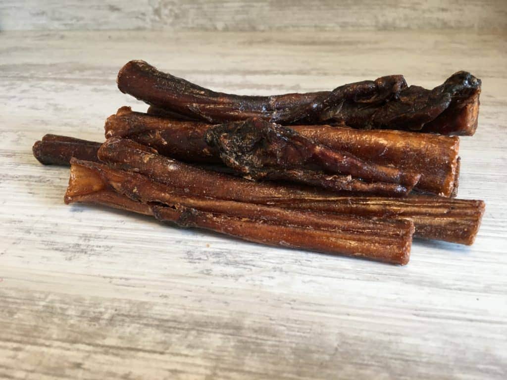Ein kleiner Haufen brauner, getrockneter Bully Sticks liegt auf einer Holzoberfläche. Die Texturen sind rau und faserig und haben ein natürliches Aussehen.