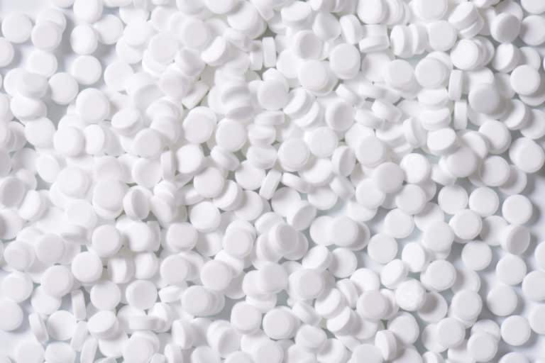 Eine Nahaufnahme zahlreicher kleiner, weißer, runder Tabletten, die über eine flache Oberfläche verstreut sind.